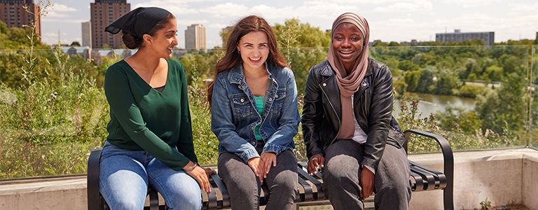 Group of female students sitting on a bench outside at Keele Campus, York University.
