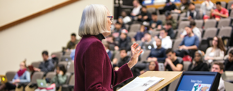 A professor stands at the podium delivering a lecture to students in Curtis Lecture Hall.