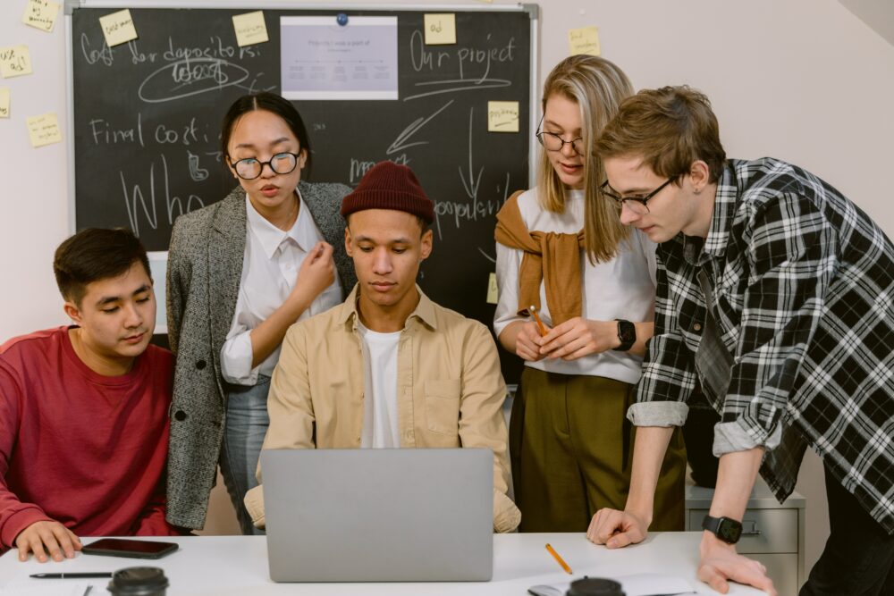 5 students look at on at a computer screen while one of them types.