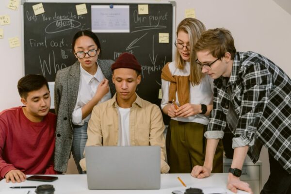 five students gather around a computer and look at the screen.