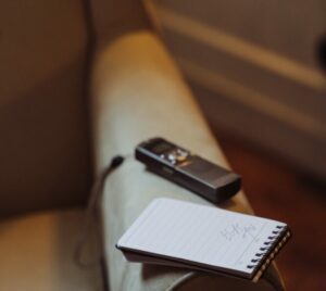 voice recorder and open notepad balancing on the arm of an empty chair